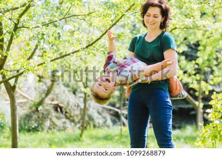 Happy laughing mother fools around and has fun in the park with her excited little son, in the garden on a summer sunny day