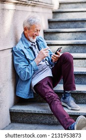 A Happy Laughing Senior Man Is Sitting On The Stairs Outdoors And Flirting On The Phone.