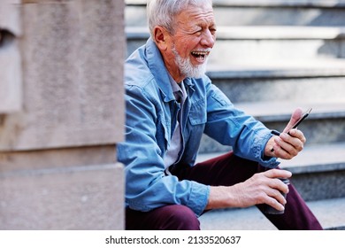 A Happy Laughing Senior Man Is Sitting On The Stairs Outdoors And Flirting On The Phone.