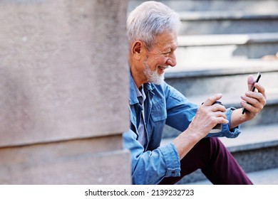 A Happy Laughing Senior Man Is Sitting On The Stairs Outdoors And Flirting On The Phone.