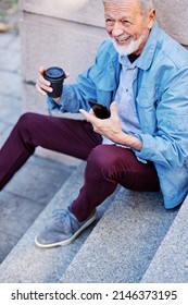 A Happy Laughing Senior Man Is Sitting On The Stairs Outdoors And Flirting On The Phone.