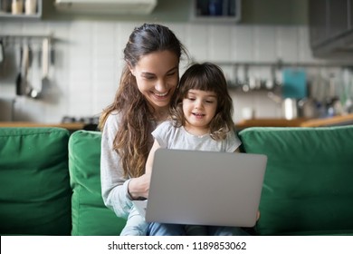 Happy laughing single mother and little preschool cute daughter using laptop online application, making video call, having fun, babysitter teaching small girl use computer, watching cartoons together