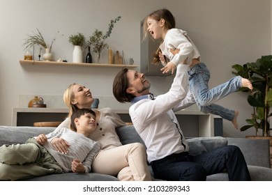 Happy laughing strong dad lifting cute little excited screaming daughter girl up in air. Cheerful couple of parents and two sibling kids, relaxing, having fun at home together. Family leisure concept
