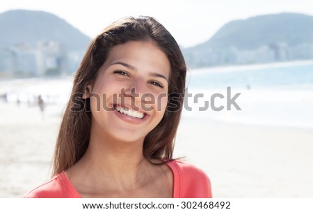 Happy laughing woman with dark hair at beach with ocean and blue sky in the background
