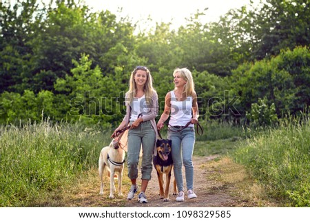 Happy laughing young women walking their dogs along a grassy rural track