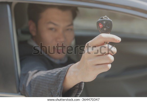 Happy learner driver asian man showing car\
key while sitting in a car (Key\
focused)