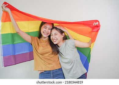 Happy lesbian, beautiful asian young two women, girl gay, couple love moment spending good time together, holding or waving lgbt rainbow, pride flag on isolated white wall background together at home. - Powered by Shutterstock