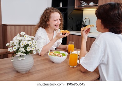 Happy Lesbian Couple Enjoying Tasty Pizza With Salad And Orange Juice For Dinner, Laughing And Discussing News