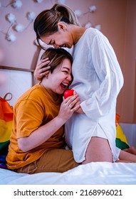 Happy lesbian couple expecting a baby. Two young beautiful women, one of them pregnant, enjoying closeness. One touches the future-mother-to-be's belly with red heart sign. Closeness concept.