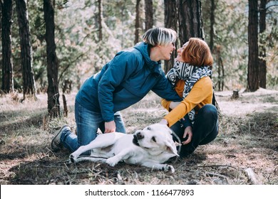 Happy Lesbian Couple Having Fun In The Forest With A Dog