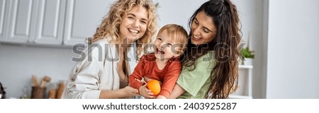 happy lesbian couple having fun together with their cute baby girl holding tangerines, banner