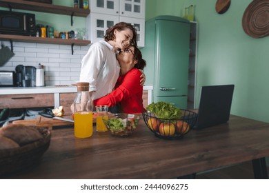 Happy lesbian couple hugging while standing in the kitchen at home. Cooking together, healthy eating concept - Powered by Shutterstock