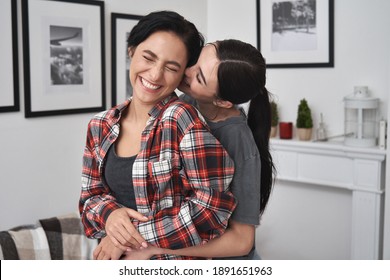 Happy lesbian lgbtq couple in love cuddling, laughing, whispering on ear having fun standing at home. Two stylish cool diverse pretty affectionate women hugging, bonding. Lgbt relationship concept - Shutterstock ID 1891651963