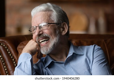 Happy life on pension. Mature aged man retiree wear glasses sit on sofa look aside laugh demonstrate healthy straight teeth prothesis implants. Old man with white smile advertise dental clinic service