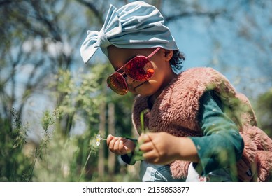 Happy Little African American Baby Girl Walking In A Park. Beautiful Black Little Girl Laughing And Playing Outside. Wearing Big Sunglasses And Playing With Flowers.