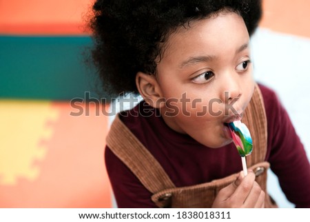 Happy little african american child boy eating candy lollipop. Black kid boy with curly hair and lollipop. Adorable black kid boy with colorful lollipop.