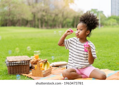 Happy little african american curly hair girl blowing soap bubbles playing alone in the park, Black hair style - Powered by Shutterstock