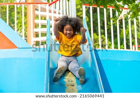 Happy Little African child girl sliding and playing at outdoor playground in the park on summer vacation. Kindergarten children kid enjoy and fun outdoor activity learning and exercising at school.