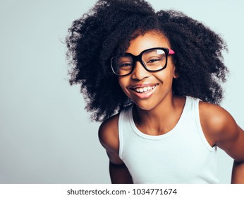 Happy little African girl with long curly hair wearing glasses while standing by herself against a gray background