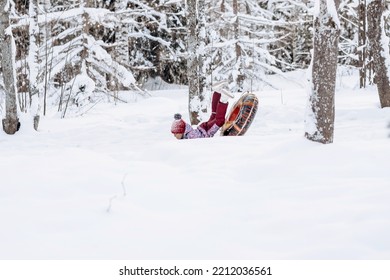 Happy Little African-American Girl In Red Hat And Jumpsuit Rides On Tubing In The Winter Park.Beautiful Trees Are Covered With White Snow.Winter Fun,active Lifestyle Concept.Selective Focus,copy Space