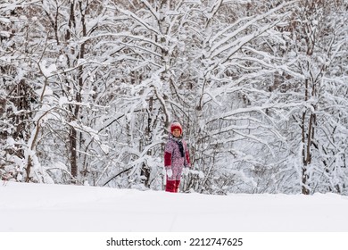 Happy Little African-American Girl In A Red Hat And Jumpsuit Walks In The Winter Forest.Beautiful Trees Are Covered With White Snow.Winter Fun,active Lifestyle Concept.Selective Focus,copy Space.