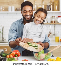 Happy Little Afro Girl And His Father Making Salad Together. Cooking With Kids Concept