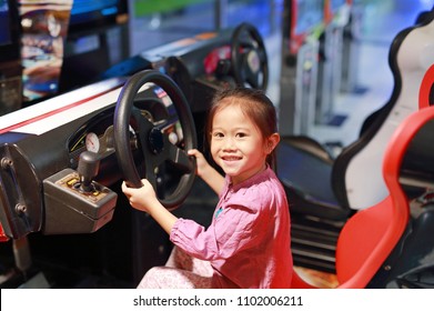 Happy little Asian child girl playing arcade video game. Racing car.