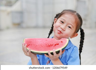 Happy Little Asian Child Girl In School Uniform Enjoy Eating Watermelon Outdoors.