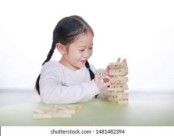 Happy Little Asian Child Girl Playing Wood Blocks Tower Game For Brain And Physical Development Skill In A Classroom. Focus At Children Face. Kid Imagination And Learning Concept.