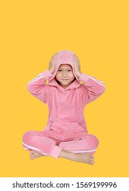 Happy little Asian child girl in pink tracksuit or sport cloth with hands touching hood on head sitting isolated on yellow background.