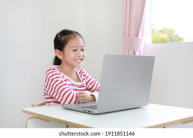 Happy Little Asian Child Girl Sitting At Desk And Using Laptop Computer