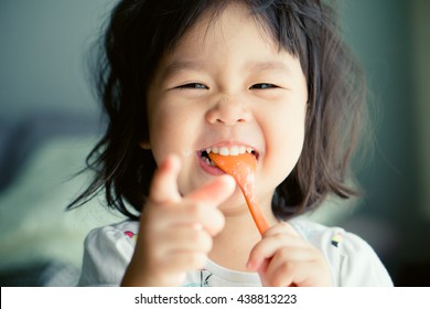 Happy Little asian child girl eating yogurt spoon in mouth.Delicious, Childhood, Baby eat food, Kid menu, Asian baby toddler girl laughing enjoy eat at home.Adorable kid looking.Baby food.Dental care.