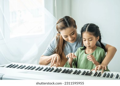 Happy little Asian deaughter playing piano with mother at home, Mother teaching daughter to play piano,They play and sing songs. They are having fun. - Powered by Shutterstock