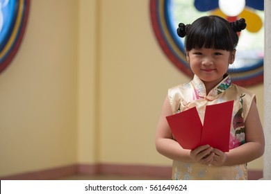 Happy Little asian girl in chinese traditional dress smiling and holding red envelope.