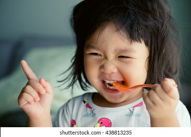 Happy Little asian girl eating yogurt and she have spoon in her mouth.