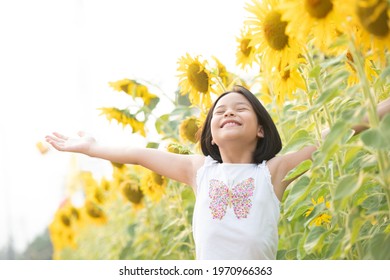 happy little asian girl having fun among blooming sunflowers under the gentle rays of the sun. child and sunflower, summer, nature and fun. summer holiday. freedom concept.