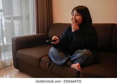 Happy Little Asian Girl Holding Remote Control And Laughing.