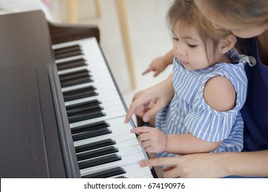 Happy Little Asian Girl Playing Piano With Mother At Home