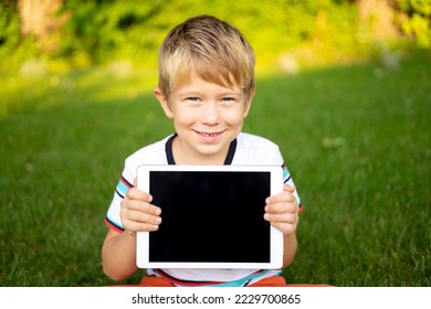 Happy little baby boy holds a tablet computer outdoors in a summer park - Powered by Shutterstock