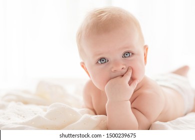 Happy little baby girl infant on a bed in white bedroom near the bright window