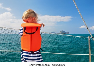 Happy Little Baby In Life Jacket On Board Of Sailing Boat Watching Offshore Sea And Tropical Islands On Summer Cruise. Children Travel Adventure On Family Vacation. Safety During Yachting With Kids.