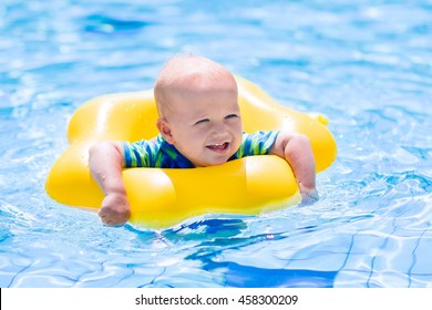 Happy little baby playing with colorful inflatable ring in outdoor swimming pool on hot summer day. Kids learn to swim. Children wearing sun protection rash guard relaxing in tropical resort - Powered by Shutterstock