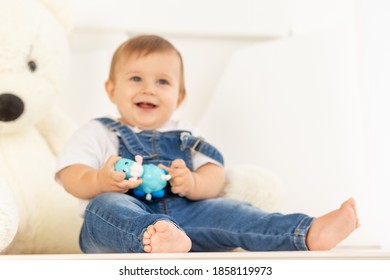 Happy Little Baby Six Months Old In Blue Jeans Sits Next To A Large Teddy Bear, Legs In Focus