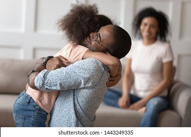 Happy little biracial girl hug loving african American dad meeting him at home after work business trip, overjoyed mixed race kid embrace black father reunited with smiling mom. Family reunion concept