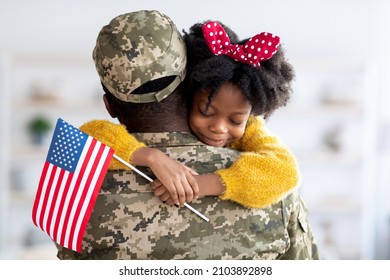 Happy Little Black Daughter Hugging Her Soldier Dad After He Came Back Home From US Army, Smiling Girl Holding American Flag And Embracing Father In Military Uniform, Celebrating Reunion With Daddy