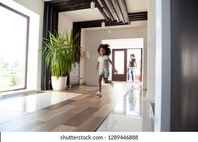Happy little black girl running exploring big luxury house moving in, parents and excited kid daughter entering new home, cute mixed race child having fun jump in hallway, african family mortgage