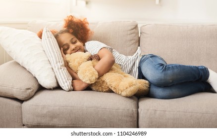 Happy Little Black Girl Sleeping With Toy On Sofa At Home. Smiling Dreamy Child Taking A Nap On Couch, Copy Space