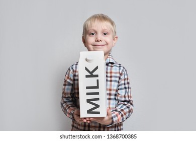 Happy Little Blond Boy Is Holding A Big White Carton Milk Package. Light Background