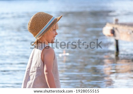 Happy little blond caucasian boy wearing straw hat stands by the river. Copy space for your text. Summer kids fun theme.