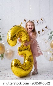 Happy Little Blond Girl In Pink Dress Holding Big Gold Foil Balloon Number And Digit Three 3